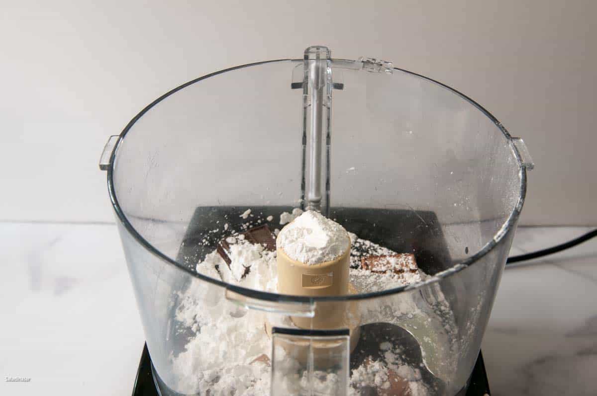 Adding sweet chocolate and powdered sugar to the food processor work bowl.