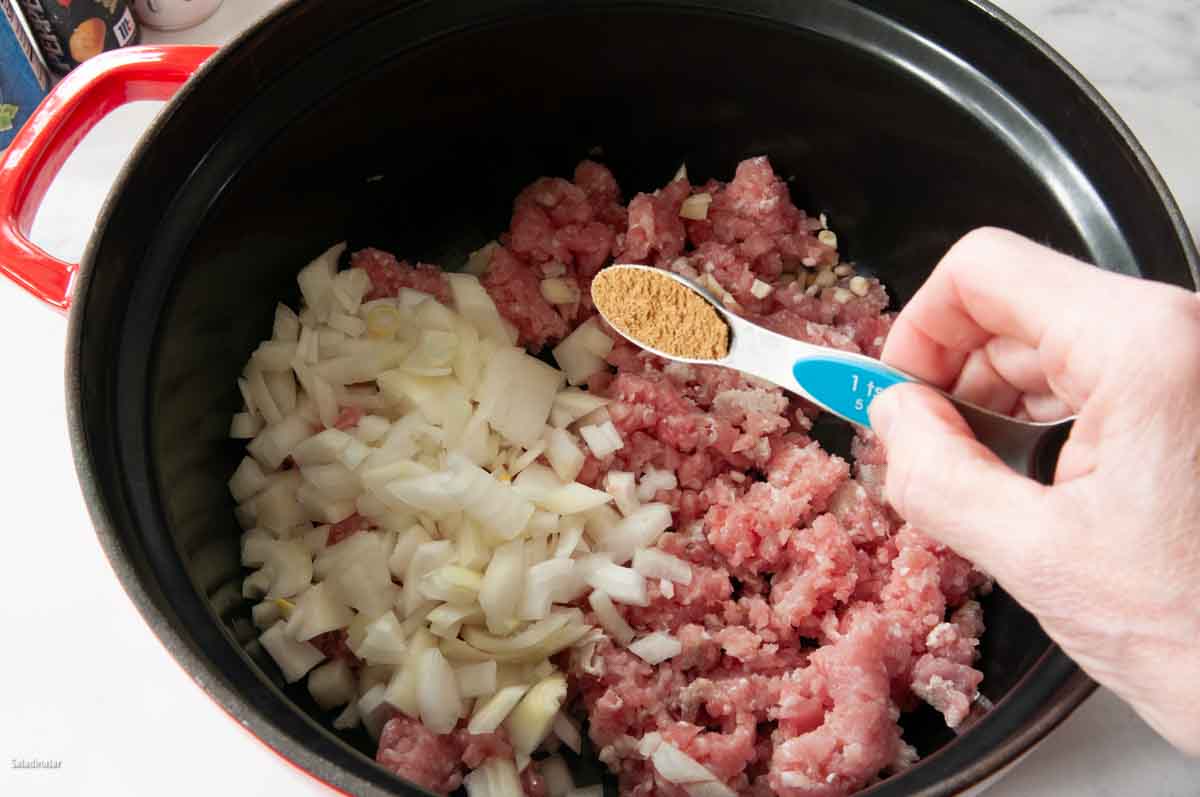 Browning the ground pork, onions, garlic clove, and cumin.