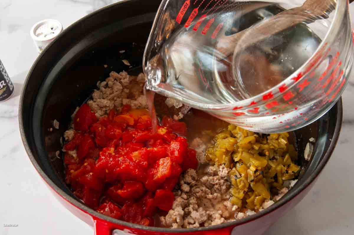 Adding tomatoes, green chiles, and water to make the stew.