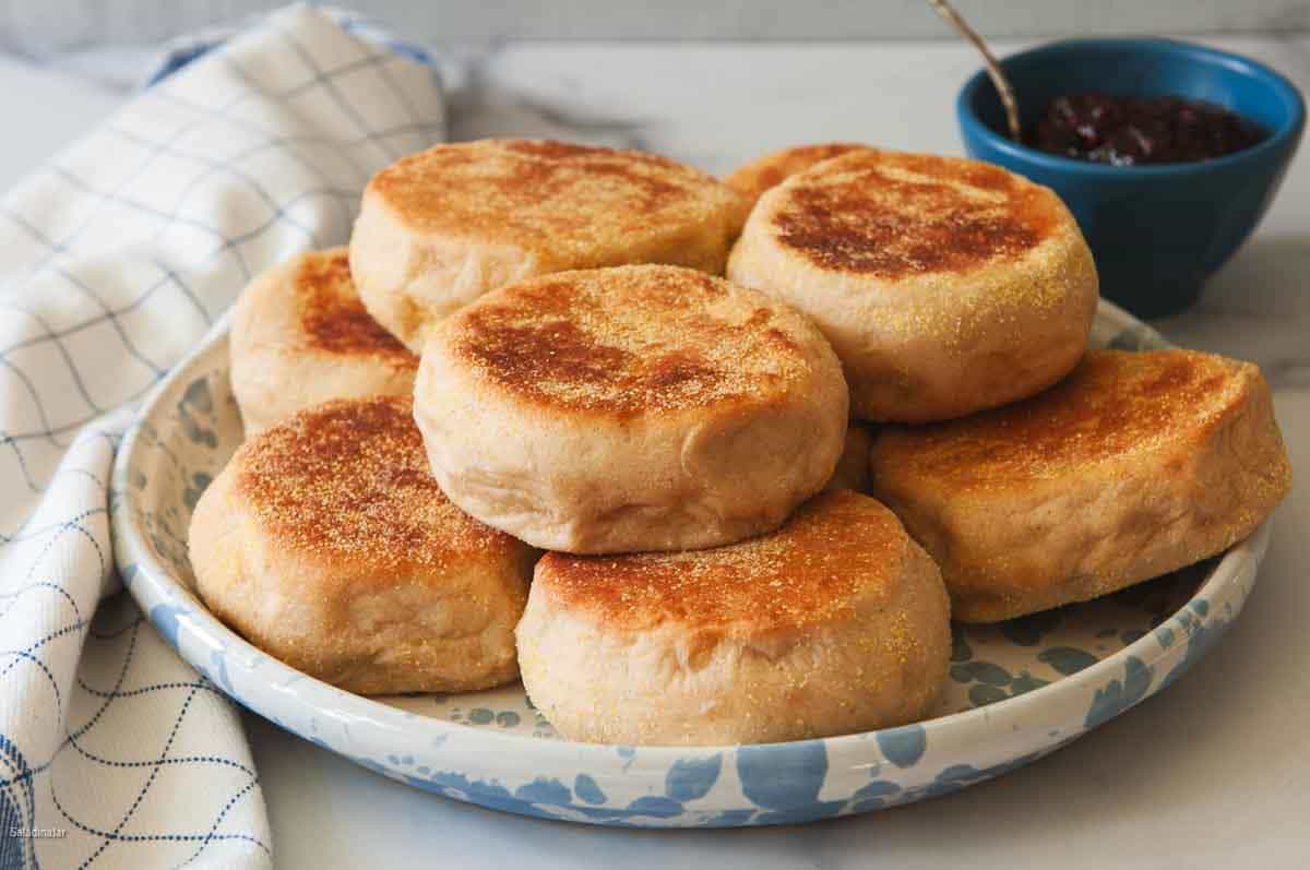 Uncut Whole wheat English Muffins on a plate with jelly on the side.