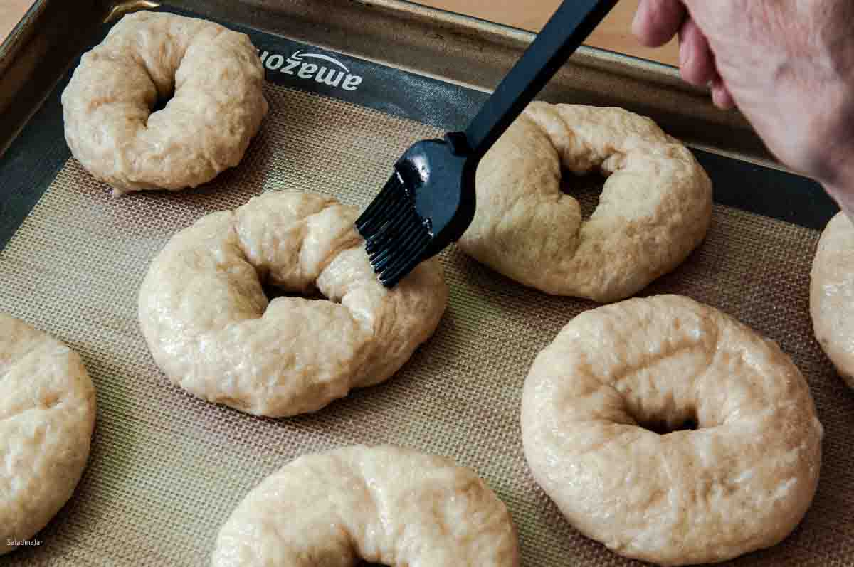 Brushing the boiled bagels with egg white glaze.