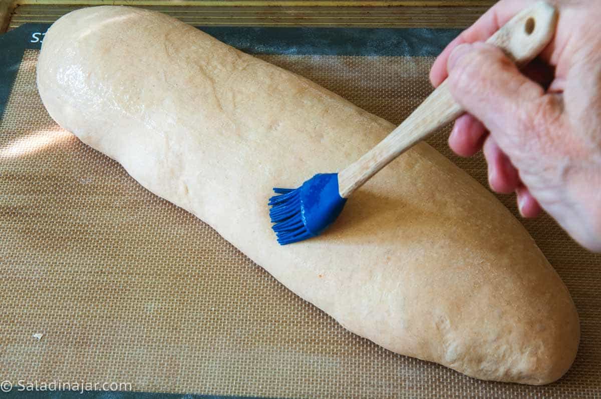 Brushing risen loaf with egg white glaze.