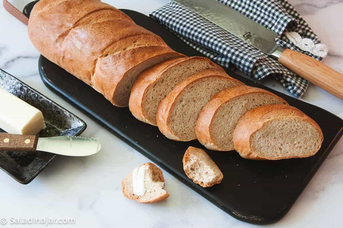 Sliced 50/50 whole wheat French bread on a cutting board, with butter on the side.