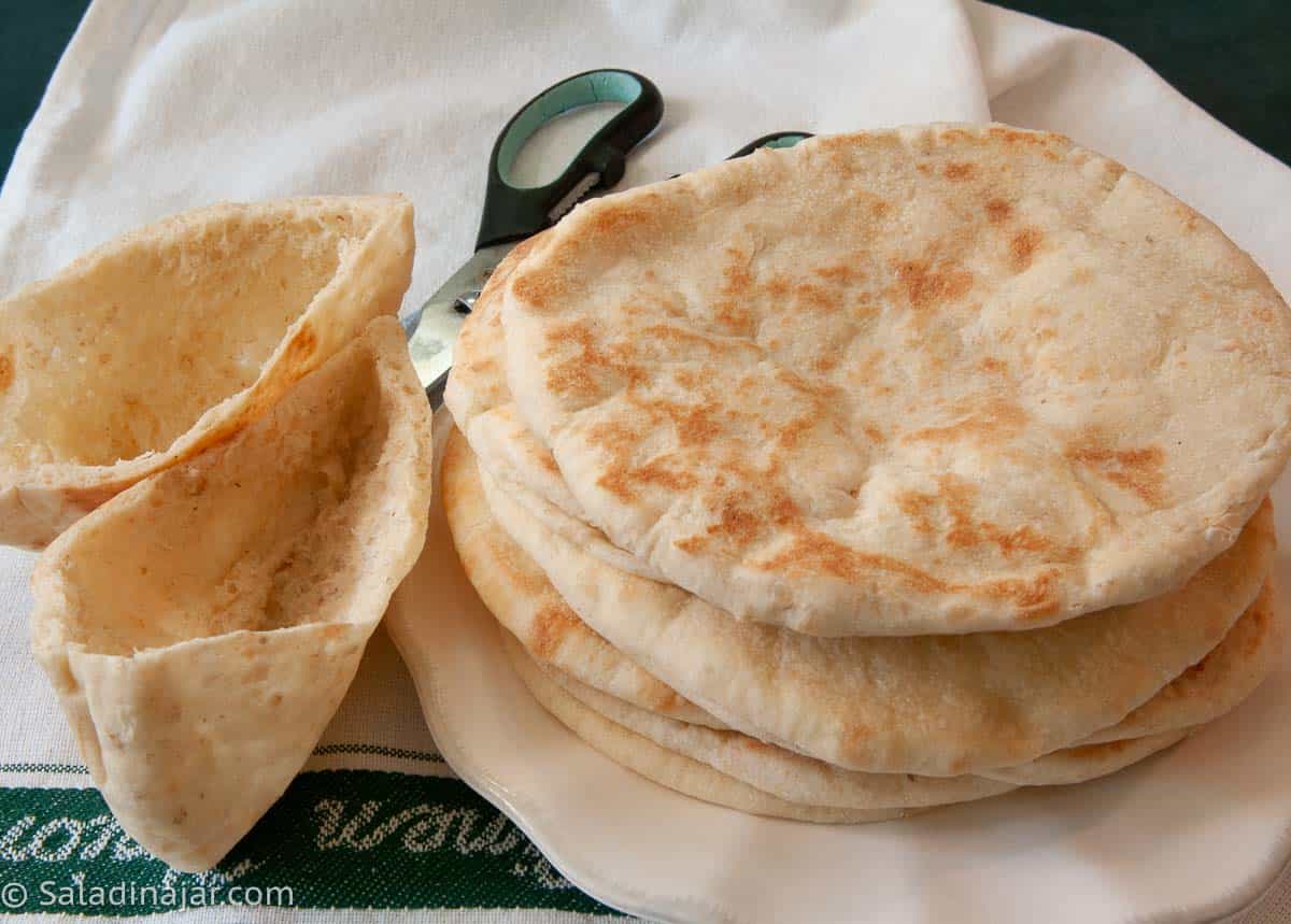 A stack of homemade bread machine pita bread with a pair of scissors in the back ground used for cutting the pita in half to make pockets